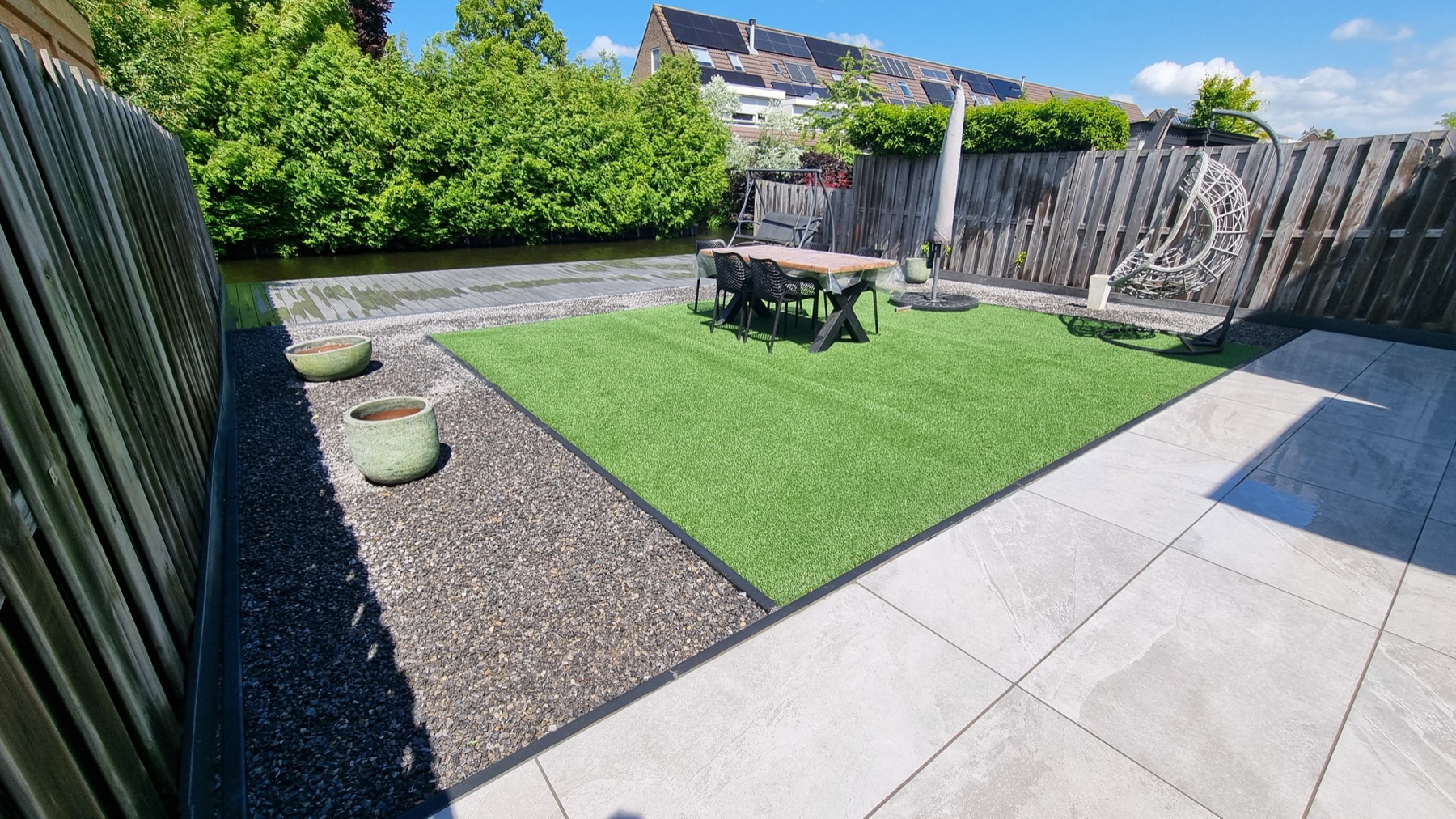 Moderne tuin met kunstgras, terras, grind en vlonder aan het water