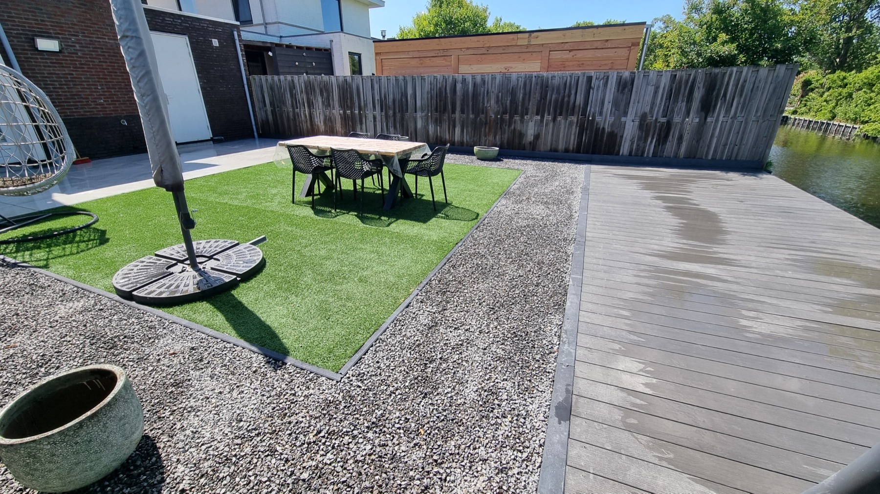 Tuin met kunstgras, grind en vlonder aan het water